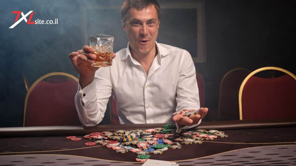 7XL POKER - שחקן קזינו מחזיק כוס משקה וז׳יטונים צבעוניים ליד שולחן פוקר עמוס בז׳יטונים, על רקע אולם אפוף עשן וכיסאות אדומים.